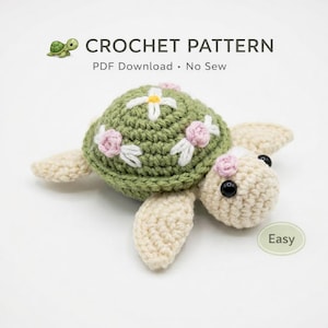 May include: A crocheted turtle with a green shell decorated with white and pink floral details. The turtle has cream-coloured flippers and head, with black eyes. The text "CROCHET PATTERN" and "PDF Download • No Sew" is visible.