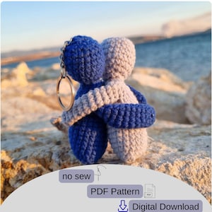 Può includere: Un portachiavi all'uncinetto con due figure che si abbracciano, una blu e una grigia, con un portachiavi argentato. Le figure si abbracciano, simboleggiando la connessione. L'immagine include il testo "no sew", "PDF Pattern" e "Digital Download".