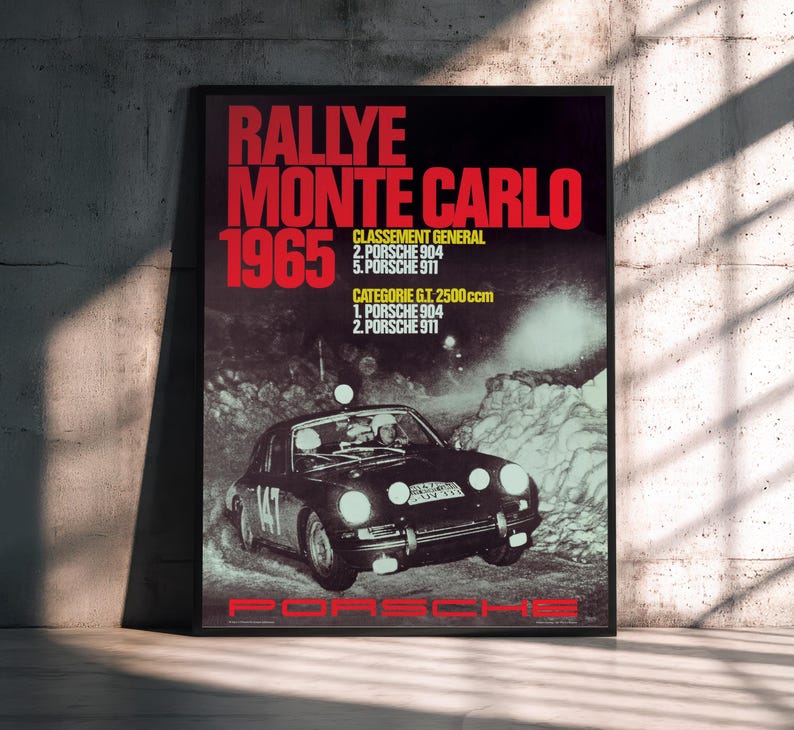 May include: A framed poster advertising the 1965 Monte Carlo Rally, featuring a Porsche race car. The poster has red text, including "RALLYE MONTE CARLO 1965" and race results. The Porsche logo is at the bottom, set against a dark background.
