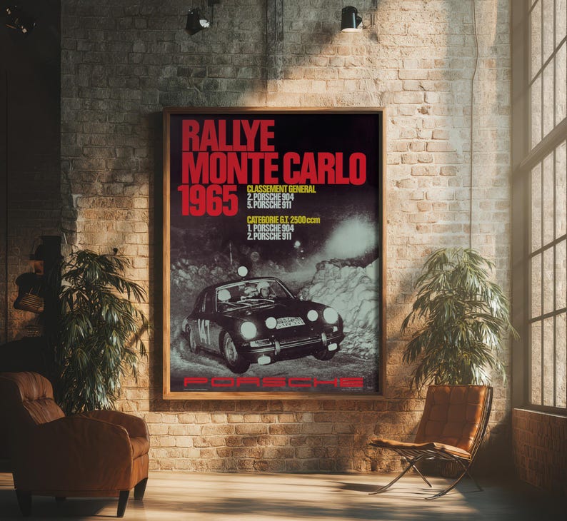 May include: A framed vintage poster with the text "RALLYE MONTE CARLO 1965" in red and white. The poster features a black Porsche race car and is displayed in a room with brick walls and a leather chair.
