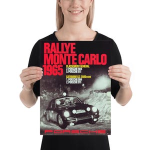 May include: Poster depicting a vintage car racing scene. The poster has the text "RALLYE MONTE CARLO 1965" in red and white. A black Porsche car is shown racing on a snowy road. The poster also lists the race results.