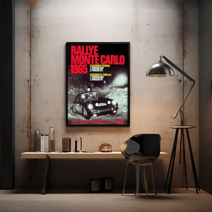 May include: A framed poster advertising the 1965 Monte Carlo Rally. The poster, with a black background and red text, shows a vintage racing car. The poster is mounted on a concrete wall, with a desk and chair in front.