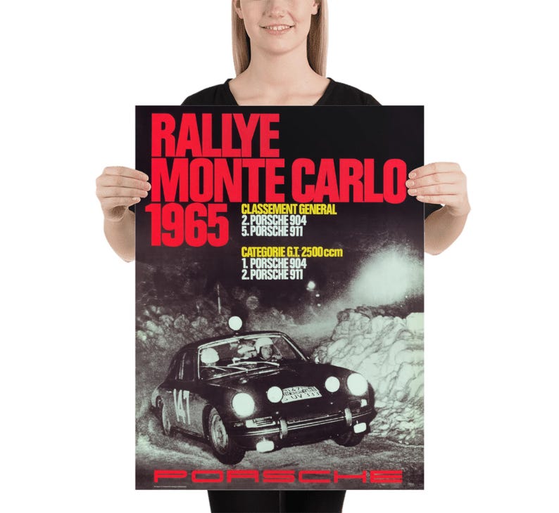 May include: Poster depicting a vintage Porsche race car in a snowy scene. The poster displays the text "RALLYE MONTE CARLO 1965" in red, with race results. The Porsche logo is at the bottom of the poster.
