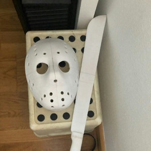 May include: A white plastic hockey mask and a white plastic machete. The mask has a black eye hole and a black nose hole. The machete has a black handle.