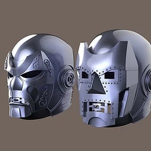 Puede incluir: Dos cascos de color plateado con detalles intrincados. Un casco tiene una forma más redondeada con un diseño detallado en la parte delantera, mientras que el otro tiene una forma más angular con un diseño más geométrico.