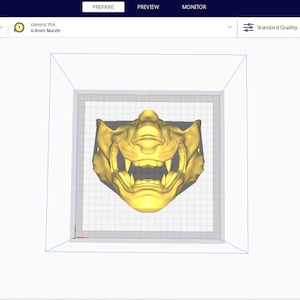 May include: A 3D model of a gold-colored mask with a fierce expression, displayed in a 3D printing software interface. The software interface shows the mask in a virtual print bed, ready to be sliced and printed.