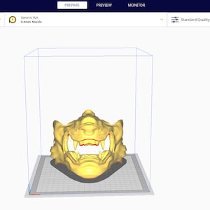 May include: A 3D model of a yellow and red detailed mask with sharp teeth, viewed from the front, in a 3D printing software program. The software interface shows the model is 172.1 x 18 x 13 mm.