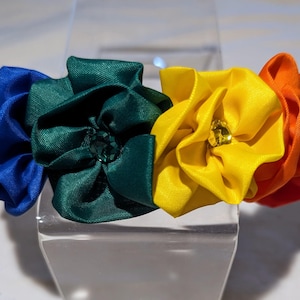 May include: A rainbow-colored headband with four fabric rosettes, each with a jewel in the center. The rosettes are blue, green, yellow, and orange.