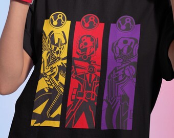 Puede incluir: Camiseta negra con un estampado gráfico de tres figuras en amarillo, rojo y morado. Cada figura lleva un casco y tiene un símbolo en el pecho.