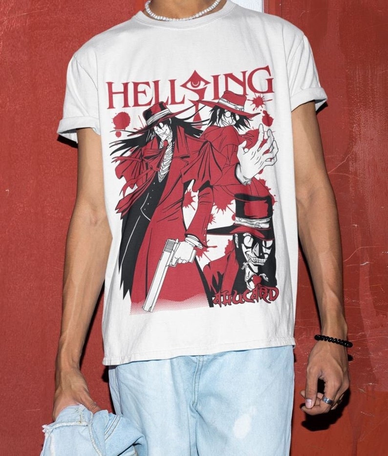 Może przedstawiać: Biała koszulka z czerwono-czarną grafiką z anime "Hellsing". Projekt przedstawia postać w czerwonym płaszczu i kapeluszu, trzymającą broń, z napisem "Hellsing" w kolorze czerwonym. Styl manga.