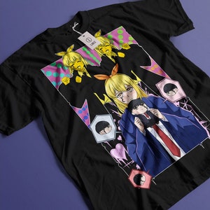 May include: Black t-shirt with a colorful graphic print featuring anime characters. The design includes a female character with yellow hair and a male character with black hair. The background is a mix of pink, green, and white polka dots.