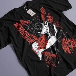Puede incluir: Camiseta negra con un gráfico de estilo anime rojo y blanco. El diseño incluye un personaje sosteniendo un arma roja, texto japonés e ilustraciones de armas rojas. Una etiqueta blanca está adjunta.
