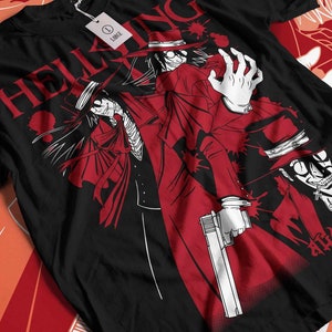 Może przedstawiać: Czarna koszulka z czerwoną grafiką postaci z anime Hellsing. Projekt przedstawia postać w długim czerwonym płaszczu, kapeluszu i trzymającą broń. Słowo "HELLSING" jest wydrukowane na g&oacute;rze na czerwono.