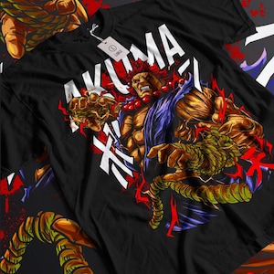 Op de afbeelding: Zwart T-shirt met een afbeelding van een gespierd, roodharig personage met een woeste uitdrukking. Het personage is omringd door Japanse karakters en bliksemschichten. De tekst "AKUMA" is in wit op het shirt gedrukt.