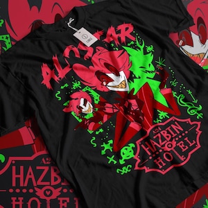 Pode incluir: Camiseta preta com uma estampa gráfica vermelha e verde de um personagem de desenho animado com o texto "ALOSTAR" e "A24 HAZBIN HOTEL".