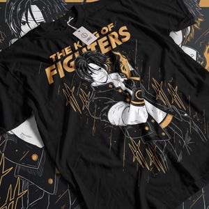 May include: Black t-shirt with a gold graphic of a character from the video game "The King of Fighters". The graphic features the character's name and a stylized design.