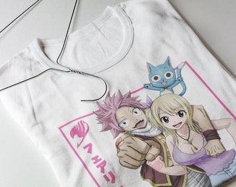 May include: White t-shirt with a pink and white graphic of three anime characters. The characters are a pink-haired boy, a blonde girl, and a blue cat. The text "Fairy Tail" is written in Japanese on the shirt.