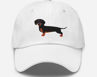 Puede incluir: Gorra de béisbol blanca con un dachshund negro y marrón bordado.