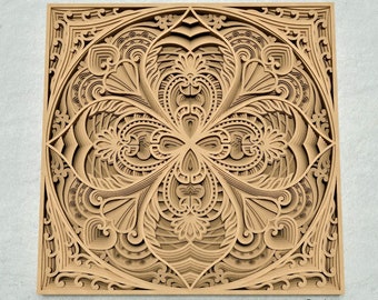 May include: A brown, intricate, laser-cut design with a square frame and a detailed, symmetrical pattern in the center. The design is reminiscent of a mandala or a flower.