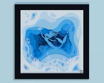 May include: A blue paper cut-out art piece depicting a mermaid swimming in an ocean scene with coral and seaweed. The art piece is framed in black and has the signature "Stei digital" in the bottom right corner.