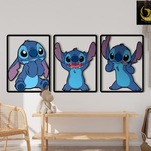 May include: Three framed wall art pieces featuring the character Stitch from Lilo & Stitch. Each piece shows Stitch in a different pose, with a blue and light blue color scheme. The frames are black, and the background is a light beige.