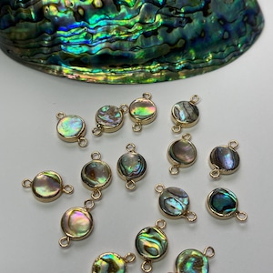 May include: A collection of 16 iridescent abalone shell round beads with gold-toned jump rings. The beads are approximately 1 inch in diameter.