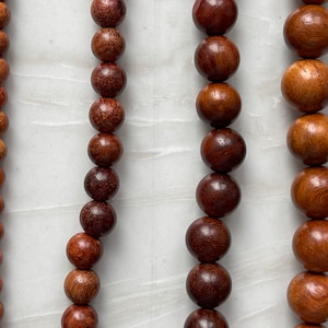 May include: Four vertical strands of round wooden beads arranged by size, ranging from small beads on the far left to large beads on the far right. Each strand features a polished, natural brown wood grain texture with varying dark and light tones.