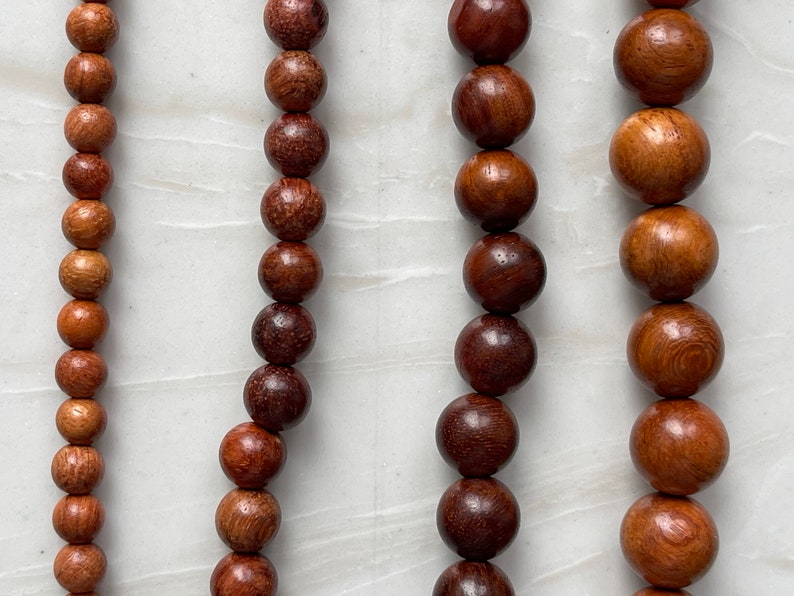 May include: Four vertical strands of round wooden beads arranged by size, ranging from small beads on the far left to large beads on the far right. Each strand features a polished, natural brown wood grain texture with varying dark and light tones.