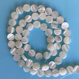 May include: A strand of white mother of pearl round beads. The beads are strung on a clear elastic cord.