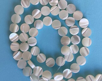 Peut inclure: Un brin de perles rondes en nacre blanche. Les perles sont enfilées sur un cordon élastique transparent.