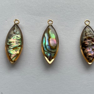 Peut inclure: Trois pendentifs dorés avec des inserts en nacre d'ormeau irisée. Les pendentifs sont en forme de goutte d'eau avec une pointe pointue et une base arrondie.