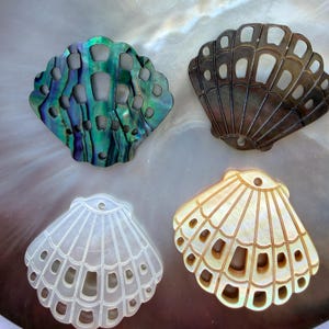 May include: Four shell-shaped pendants crafted from iridescent shell material. Each pendant features a scalloped edge and a series of cut-out rectangular windows. The colours include a deep green and purple, a dark brown, a translucent white, and a warm gold.