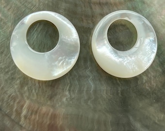 May include: Two white mother of pearl round rings with a smooth, polished finish. The rings have a large hole in the center.
