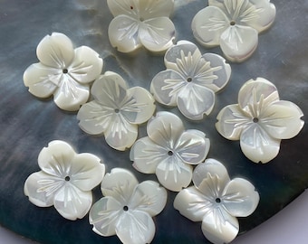 May include: Ten white mother of pearl flower shaped buttons with a carved design. The buttons have a hole in the center.