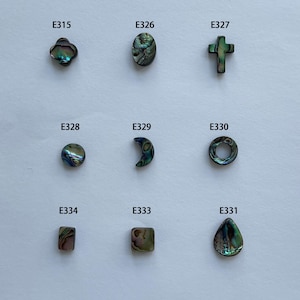 Könnte beinhalten: Neun schillernde Abalone-Muschelperlen in verschiedenen Formen: Kleeblatt, Oval, Kreuz, Kreis, Halbmond und Tropfen. Jede Perle ist mit einem eindeutigen Code versehen. Die Perlen haben grüne, blaue und violette Farbtöne.