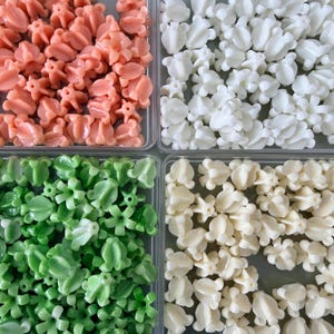 May include: Overhead shot of four compartments filled with decorative beads. The beads are in shades of peach, white, green, and cream. Each bead has a unique floral design, perfect for jewelry making or craft projects.