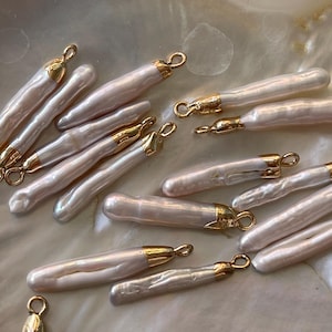 Könnte beinhalten: Eine Sammlung von 12 weißen Barockperlen-Anhängern mit goldfarbenen Sprungringen. Die Perlen sind unregelmäßig geformt und haben ein natürliches, organisches Aussehen.