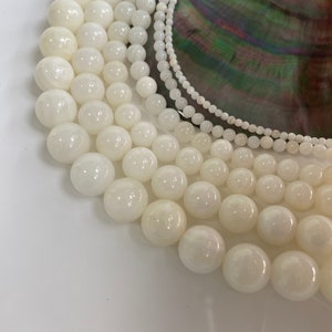 Puede incluir: Una colección de cuentas redondas blancas de diferentes tamaños, dispuestas en semicírculo sobre una superficie blanca.