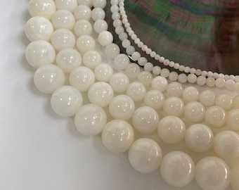 May include: A collection of white round beads of varying sizes, arranged in a semi-circle on a white surface.