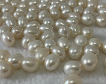 May include: A collection of white oval-shaped pearls, scattered on a white surface.