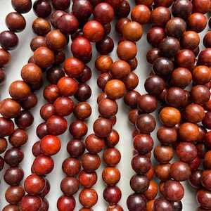 May include: A collection of round, polished wooden beads in various shades of deep reddish-brown and dark brown. The beads are arranged in multiple vertical strands, showcasing natural wood grain patterns and a smooth, uniform spherical shape.