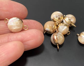 May include: A group of six round, white and gold shell beads with gold metal loops. The beads have a natural, iridescent finish.