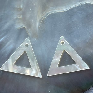 May include: Two white triangle-shaped earrings with a smaller triangle cutout in the centre. The earrings are made of mother of pearl.