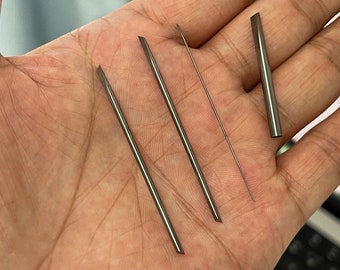 May include: Four silver metal tools, including three long, thin, pointed tools and one shorter, thicker tool with a rounded tip. The tools are arranged on a person's hand.