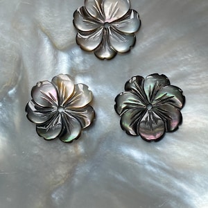 May include: Three black and iridescent mother of pearl flower-shaped buttons with a carved design.