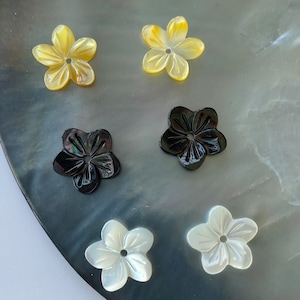Könnte beinhalten: Sechs geschnitzte, blumenförmige Knöpfe in drei Farben: Weiß, Schwarz und Gelb. Die Knöpfe sind aus Perlmutt und haben ein Loch in der Mitte.