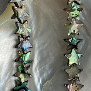 Può includere: Una collana di perle a forma di stella in madreperla di abalone iridescente. Le perle sono di un profondo verde, blu e viola con un bagliore perlaceo.