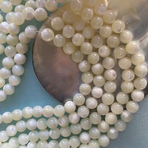 Könnte beinhalten: Eine Strähne weißer, irisierender runder Perlen aus Perlmutt auf hellblauem Hintergrund.