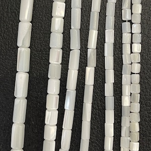 Può includere: Una collana di perline di conchiglia bianca di forma rettangolare. Le perline hanno una finitura madreperlacea e sono infilate su un filo trasparente.