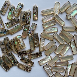 May include: A collection of iridescent rectangular shell charms with gold-toned metal frames. The charms have a variety of patterns and colors, including white, gold, and brown.